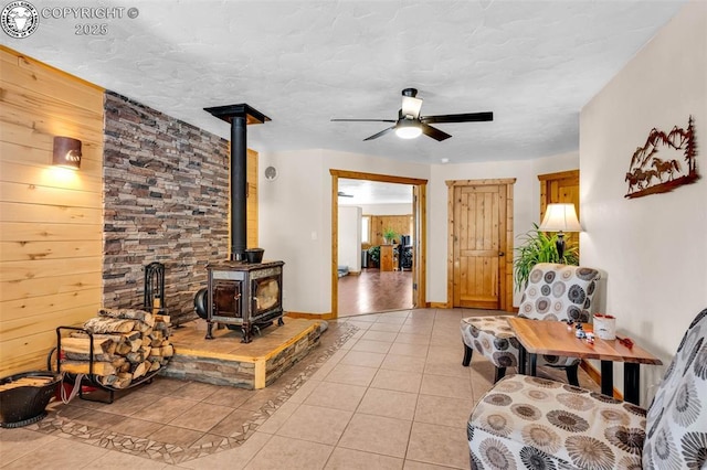 living room featuring light tile patterned floors, a textured ceiling, a wood stove, and a ceiling fan