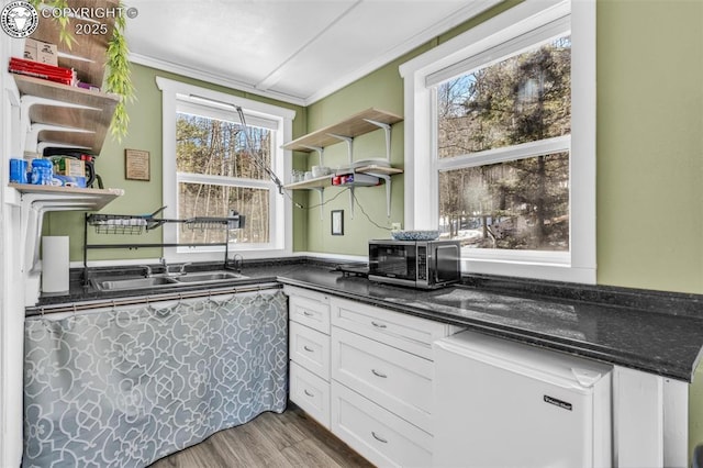 kitchen featuring light wood-type flooring, ornamental molding, open shelves, stainless steel microwave, and white cabinets