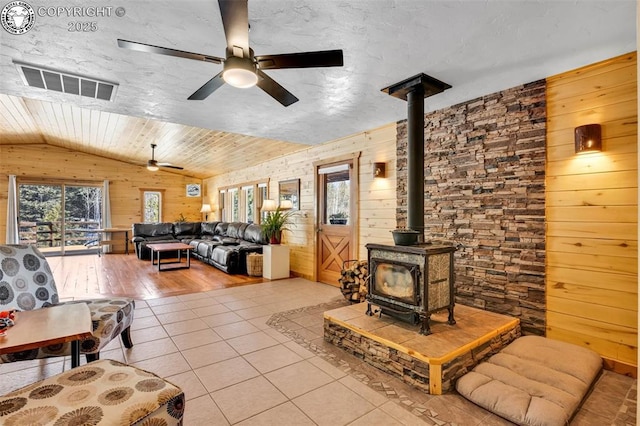 living area with visible vents, lofted ceiling, a wood stove, wood walls, and tile patterned floors