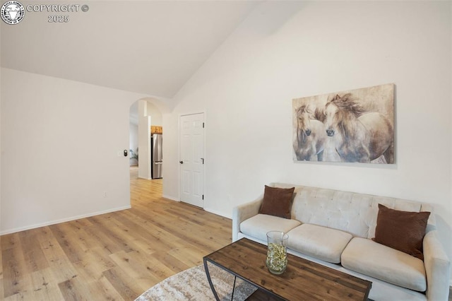 living area with baseboards, arched walkways, light wood-style flooring, and high vaulted ceiling