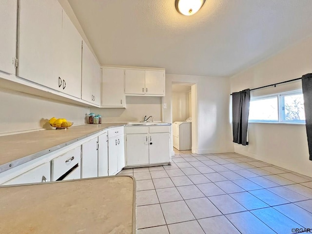 kitchen with washer / clothes dryer, white cabinetry, sink, light tile patterned floors, and a textured ceiling