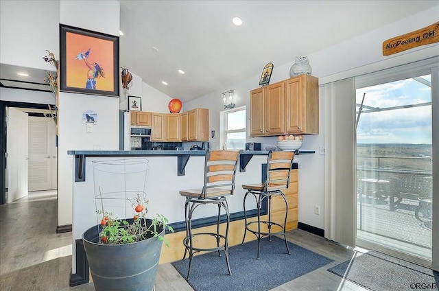 kitchen featuring lofted ceiling, backsplash, a kitchen breakfast bar, kitchen peninsula, and light wood-type flooring