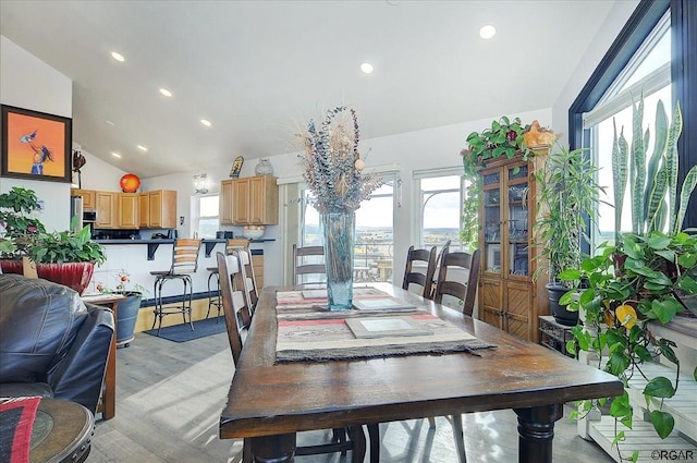 dining room featuring a healthy amount of sunlight, vaulted ceiling, and light wood-type flooring