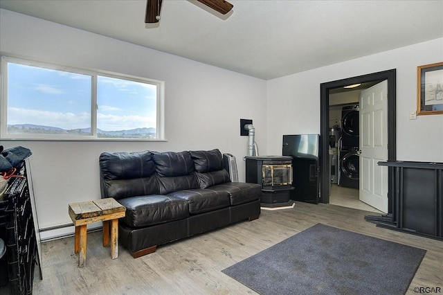 living room with ceiling fan, a baseboard radiator, stacked washer and clothes dryer, and light hardwood / wood-style floors