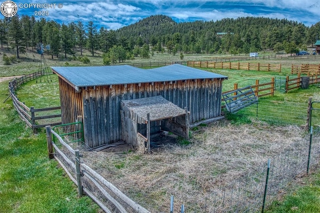 view of outdoor structure with a rural view, a view of trees, an outdoor structure, and fence