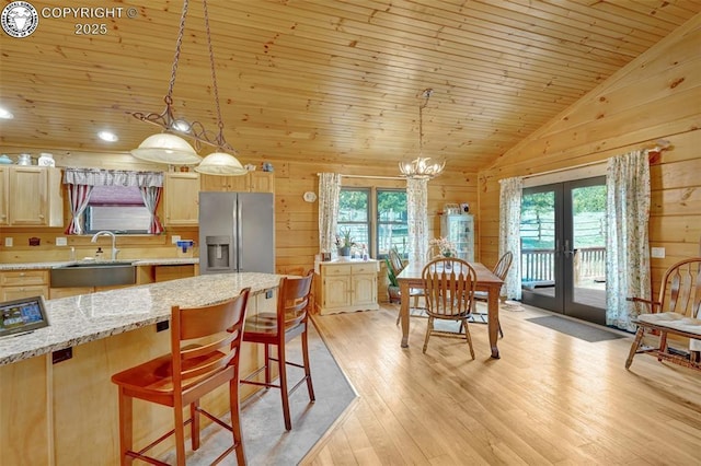 kitchen featuring light brown cabinets, stainless steel refrigerator with ice dispenser, a sink, french doors, and wood walls