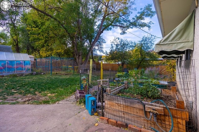 view of yard with a greenhouse, a garden, a fenced backyard, and an outbuilding