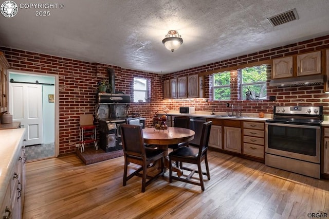 kitchen with stainless steel appliances, visible vents, a wood stove, a sink, and brick wall