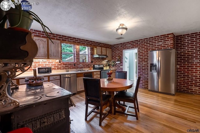 kitchen featuring brick wall, a sink, light countertops, appliances with stainless steel finishes, and light wood finished floors