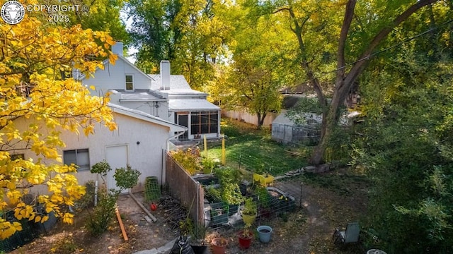 rear view of house featuring a vegetable garden, a sunroom, a chimney, fence, and stucco siding