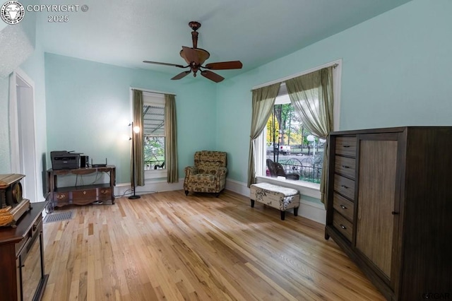 living area with a healthy amount of sunlight, light wood finished floors, baseboards, and a ceiling fan