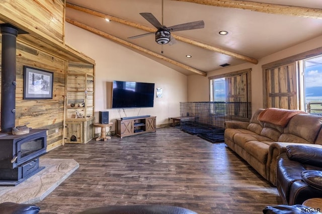 living room with wooden walls, a wood stove, vaulted ceiling with beams, ceiling fan, and dark wood-type flooring