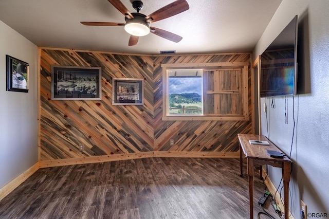 interior space with dark wood-type flooring, ceiling fan, and wood walls