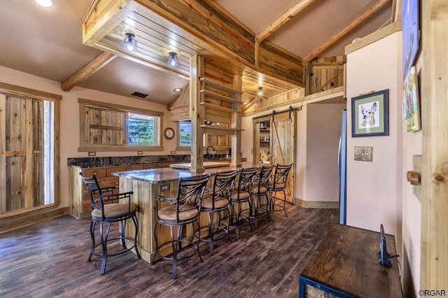 kitchen featuring a barn door, vaulted ceiling with beams, a breakfast bar area, and dark hardwood / wood-style flooring