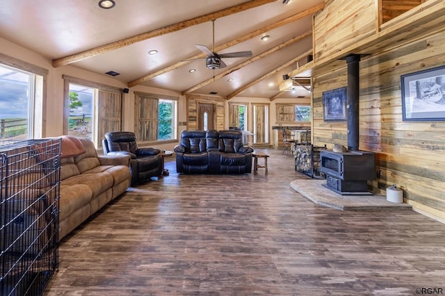 living room with vaulted ceiling with beams, wood walls, a wood stove, dark hardwood / wood-style flooring, and ceiling fan