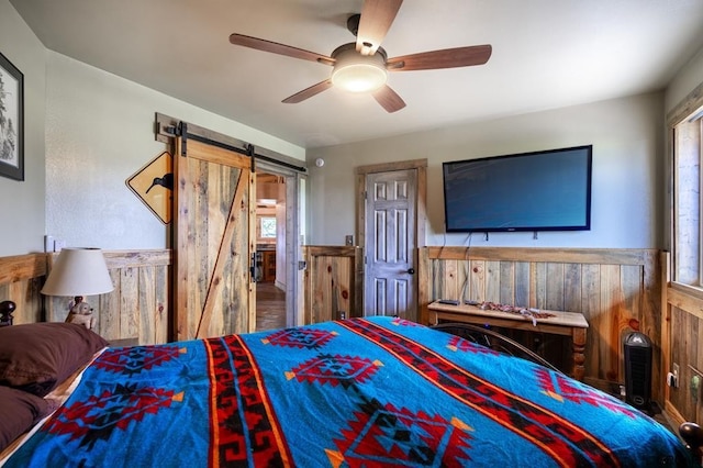 bedroom featuring a barn door, ceiling fan, and wood walls