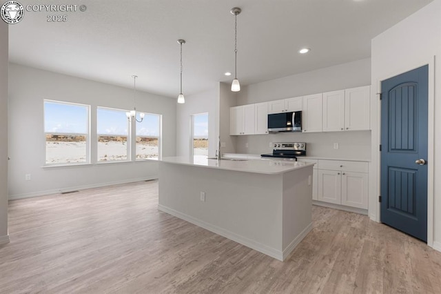 kitchen with sink, white cabinetry, a kitchen island with sink, stainless steel appliances, and decorative light fixtures