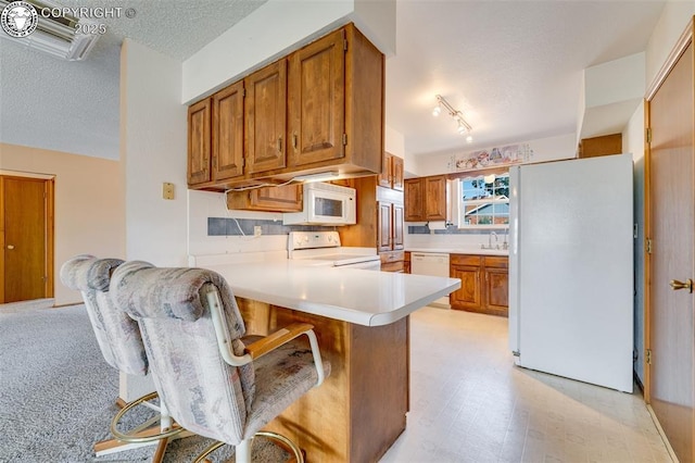 1108 Fairview Ave Unit B, Canon City, CO 81212 - kitchen with white appliances, a peninsula, a textured ceiling, brown cabinetry, and light countertops