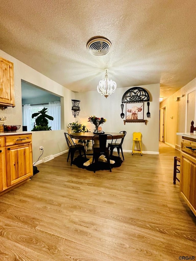 dining space with light hardwood / wood-style flooring, a textured ceiling, and a notable chandelier