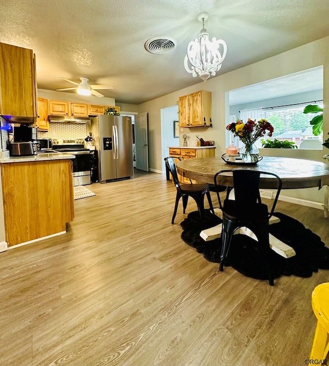 dining area featuring ceiling fan with notable chandelier, light hardwood / wood-style floors, and a textured ceiling