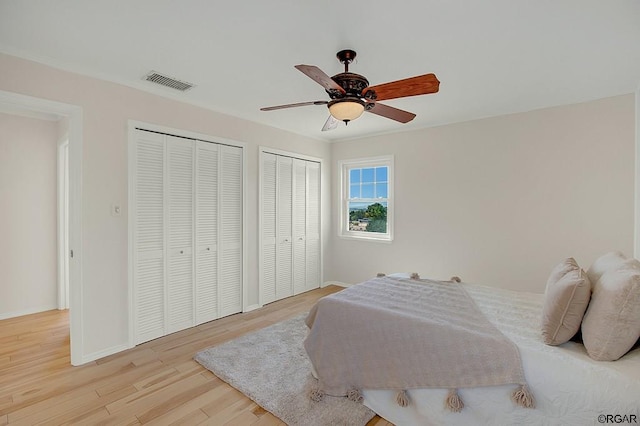 bedroom featuring two closets, light hardwood / wood-style floors, and ceiling fan