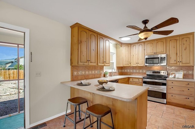 kitchen with light tile patterned flooring, sink, a kitchen breakfast bar, kitchen peninsula, and stainless steel appliances