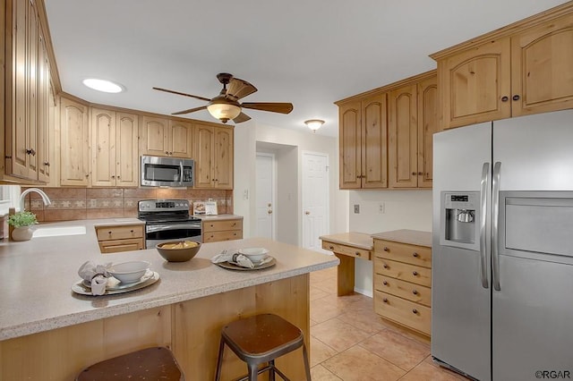 kitchen with appliances with stainless steel finishes, sink, a kitchen breakfast bar, light tile patterned floors, and kitchen peninsula