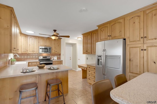 kitchen featuring sink, ceiling fan, appliances with stainless steel finishes, a kitchen bar, and light tile patterned flooring