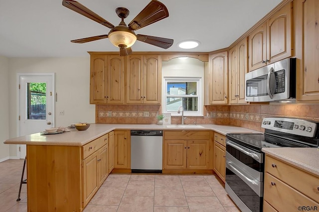 kitchen with sink, light tile patterned floors, light brown cabinets, appliances with stainless steel finishes, and decorative backsplash