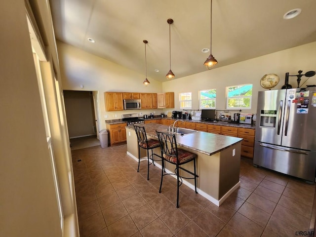 kitchen with dark tile patterned floors, hanging light fixtures, a kitchen breakfast bar, stainless steel appliances, and an island with sink