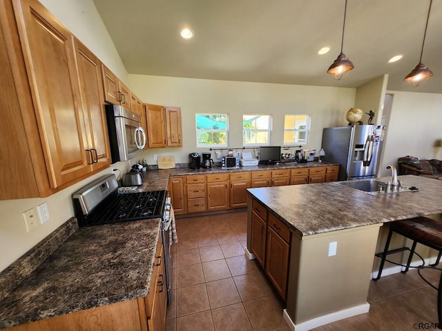 kitchen featuring sink, a kitchen island with sink, stainless steel appliances, dark tile patterned flooring, and decorative light fixtures