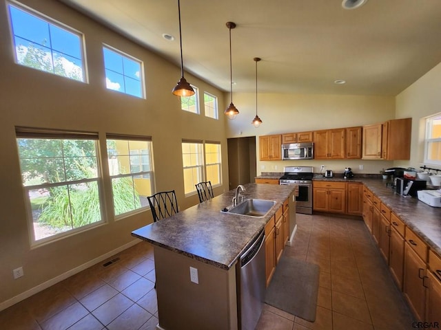 kitchen with sink, appliances with stainless steel finishes, dark tile patterned flooring, pendant lighting, and a kitchen island with sink