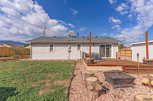 rear view of house featuring a wooden deck, central AC, a fire pit, and a lawn