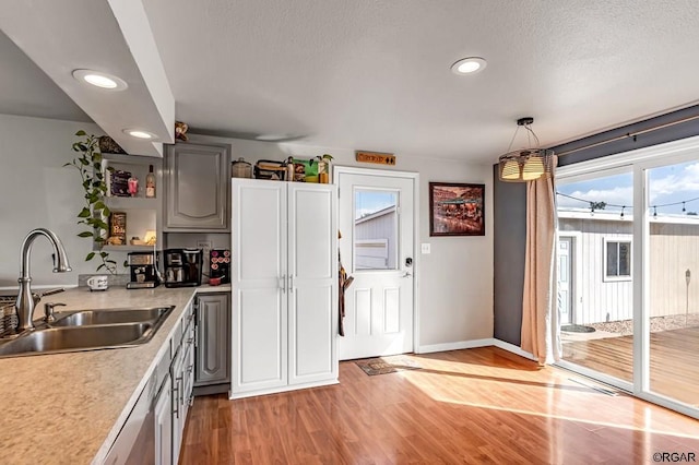 kitchen featuring gray cabinets, sink, hanging light fixtures, a textured ceiling, and light hardwood / wood-style flooring