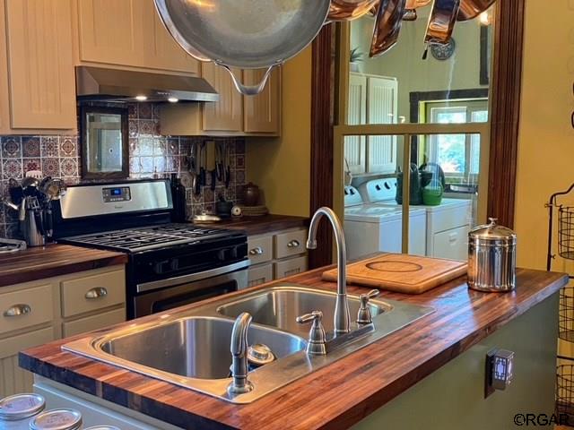 kitchen featuring washing machine and clothes dryer, stainless steel range with gas stovetop, extractor fan, and butcher block countertops