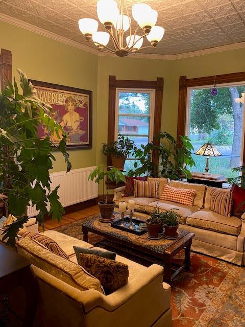 living room featuring hardwood / wood-style flooring, crown molding, radiator heating unit, and a chandelier