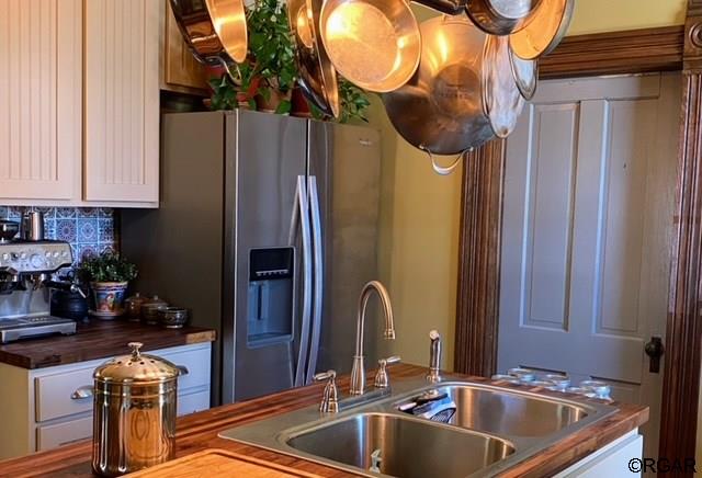 kitchen with stainless steel refrigerator with ice dispenser, white cabinetry, sink, and decorative backsplash