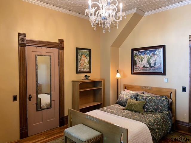 bedroom with crown molding, a notable chandelier, and hardwood / wood-style flooring