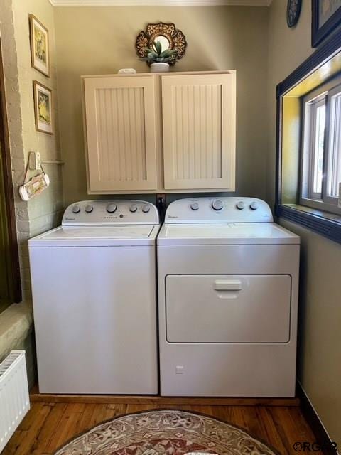 washroom featuring cabinets, radiator, washing machine and clothes dryer, and dark hardwood / wood-style flooring