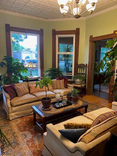 living room featuring crown molding, wood-type flooring, and an inviting chandelier