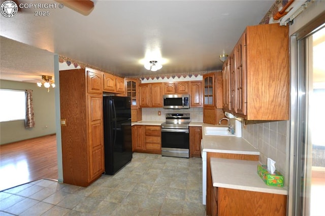 kitchen featuring brown cabinetry, a ceiling fan, appliances with stainless steel finishes, tasteful backsplash, and a sink