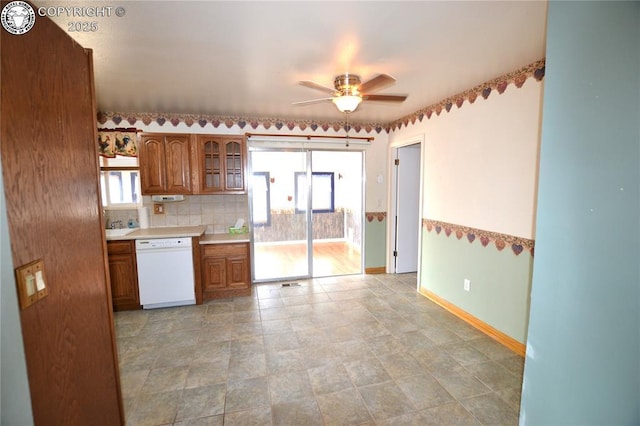 kitchen featuring ceiling fan, dishwasher, brown cabinetry, baseboards, and glass insert cabinets