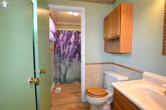 bathroom featuring vanity, visible vents, toilet, tile walls, and a wainscoted wall