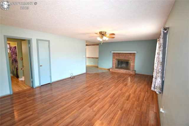 unfurnished living room with ceiling fan, a fireplace, light wood-type flooring, and a textured ceiling