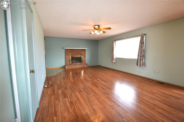 unfurnished living room with visible vents, a ceiling fan, wood finished floors, and a brick fireplace