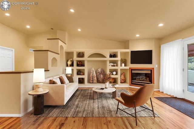 living room with vaulted ceiling, built in features, and light hardwood / wood-style flooring