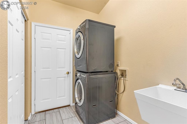 clothes washing area featuring stacked washing maching and dryer, sink, and light tile patterned floors