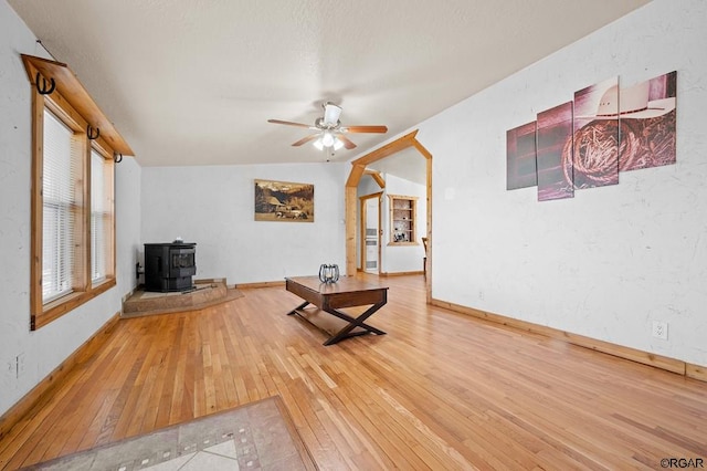 unfurnished living room with lofted ceiling, hardwood / wood-style flooring, ceiling fan, and a wood stove