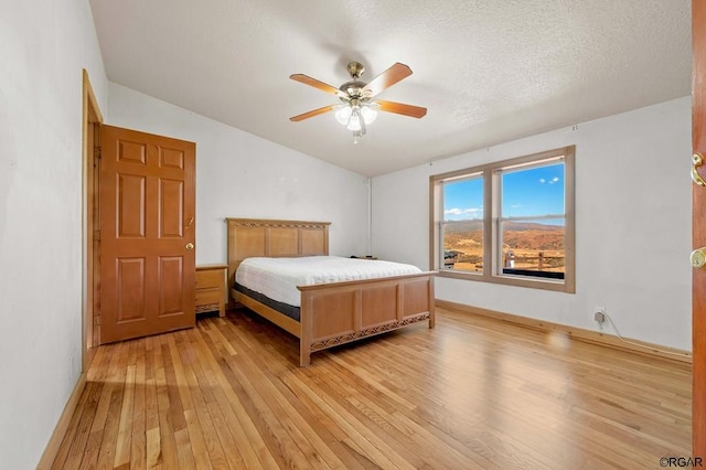 bedroom featuring vaulted ceiling, a textured ceiling, ceiling fan, and light hardwood / wood-style flooring