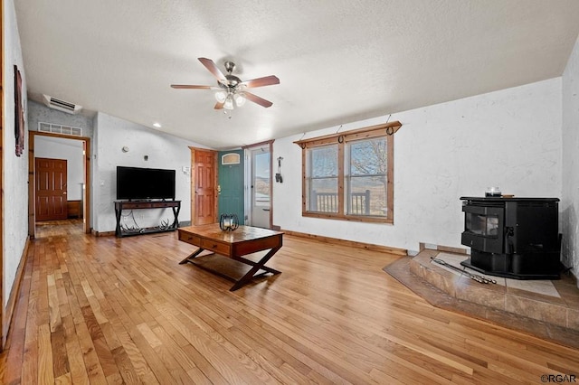 living room featuring vaulted ceiling, a textured ceiling, a wood stove, ceiling fan, and light hardwood / wood-style floors